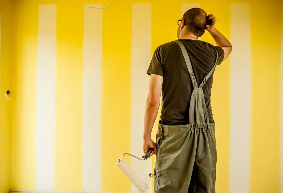 Painter with a roller looking over a yellow striped wall