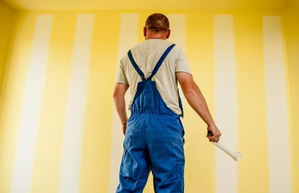Painter in overalls standing in front of a freshly striped yellow wall